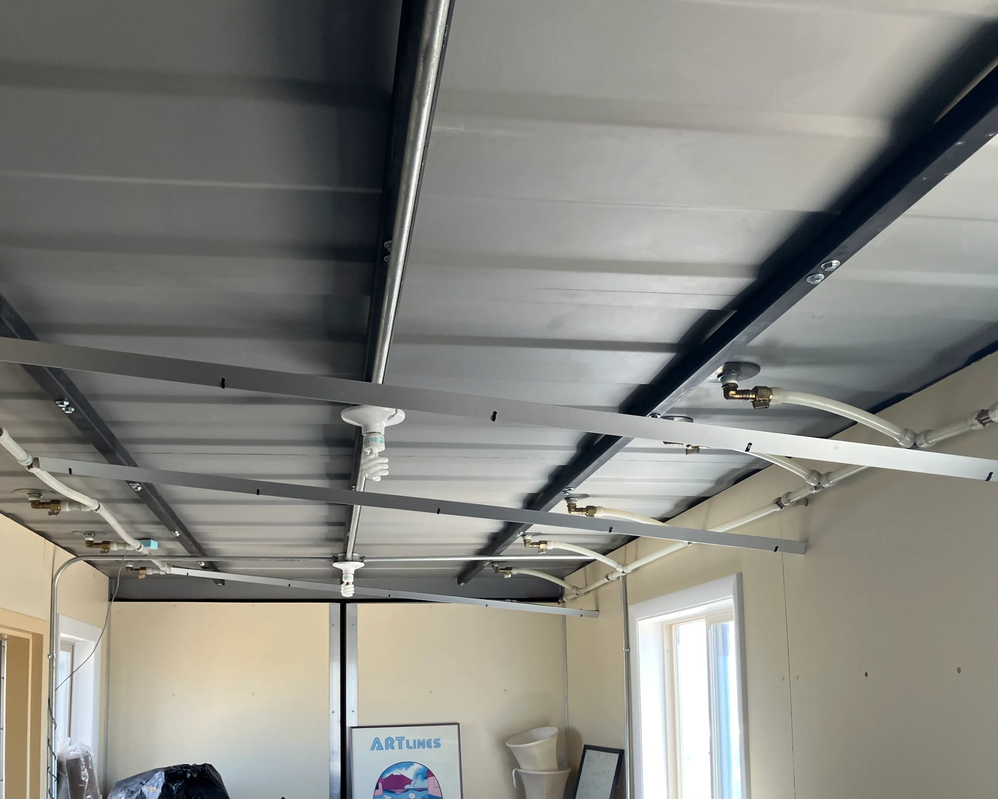 Interior view looking up at the Double Play ceiling, showing white push-fit tubing running to several brass manifold fittings across the structural beams